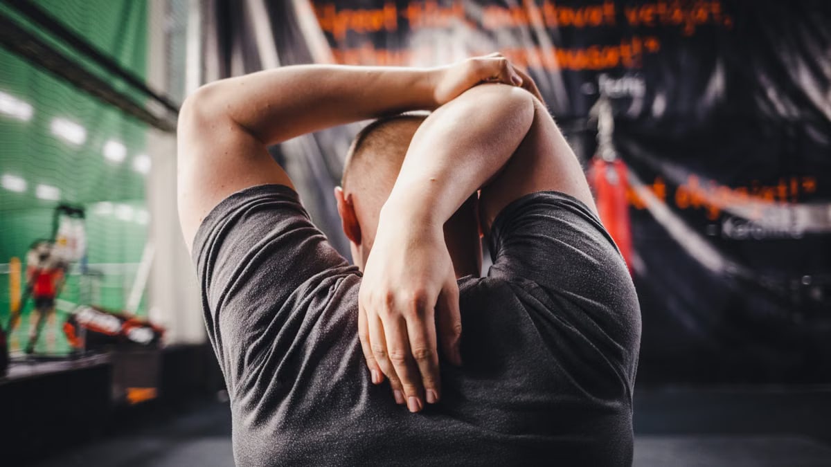 Man stretching arms in a gym, viewed from behind, focusing on fitness and flexibility.